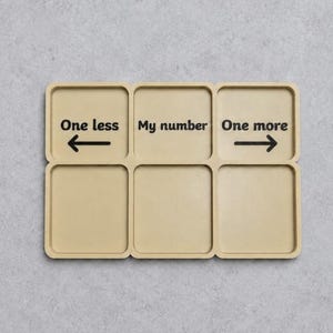 May include: A beige rectangular tray with six compartments. The top row features black text and arrows: 'One less' with a left arrow, 'My number' in the centre, and 'One more' with a right arrow. The bottom row consists of three empty compartments.