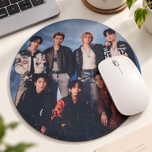 May include: A round mouse pad featuring a high-resolution group photograph of seven individuals dressed in casual jackets and shirts against a blue background. A white computer mouse rests on the right side of the circular pad surface.