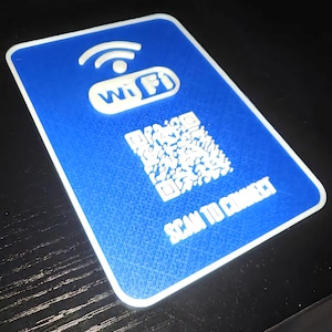 Könnte beinhalten: Eine blaue rechteckige Karte mit weißem Rand. Die Karte zeigt ein weißes Wi-Fi-Symbol und das Wort "Wi-Fi". Ein QR-Code und der Text "SCAN TO CONNECT" sind ebenfalls auf der Karte zu sehen.