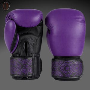 May include: A pair of purple and black boxing gloves featuring a perforated palm area and a wrist strap decorated with a repeating purple floral pattern. The logo Punching Bags Heaven is visible in the upper left corner of the image.