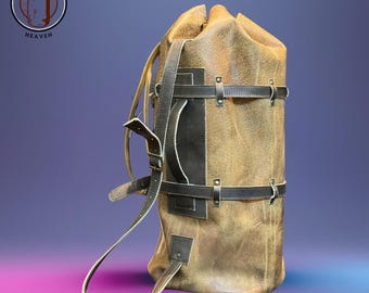 Könnte beinhalten: Ein brauner Leder-Boxsack mit schwarzen Riemen und Akzenten. Die Tasche hat einen Kordelzugverschluss oben und einen Griff an der Seite. Die Tasche ist zylindrisch und hat ein Used-Finish. Das Logo "PUNCHING BAGS HEAVEN" ist oben links sichtbar.
