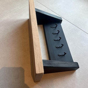 May include: A wooden key rack with a natural wood side and a black painted body. It has six metal hooks for keys. The design is simple and functional, suitable for hallway or entryway organization.