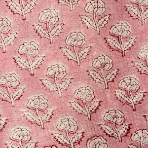 May include: Close-up of a pink fabric featuring a repeating floral design. The flowers are white with red outlines and stems, set against a soft pink backdrop. The fabric has a slightly textured appearance.