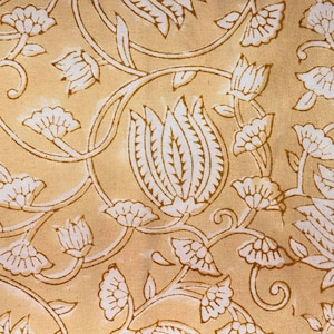 May include: Close-up of a fabric with a repeating floral pattern. The design features white flowers and leaves with brown outlines on a light yellow background. The pattern includes large tulip-like shapes and smaller, more delicate blossoms.