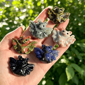 Puede incluir: Una colecci&oacute;n de peque&ntilde;as figuras de murci&eacute;lagos talladas en varios colores y patrones. Los murci&eacute;lagos est&aacute;n hechos de diferentes tipos de piedra, incluyendo negro, verde, azul y blanco. Cada murci&eacute;lago tiene alas detalladas y ojos peque&ntilde;os y redondos.