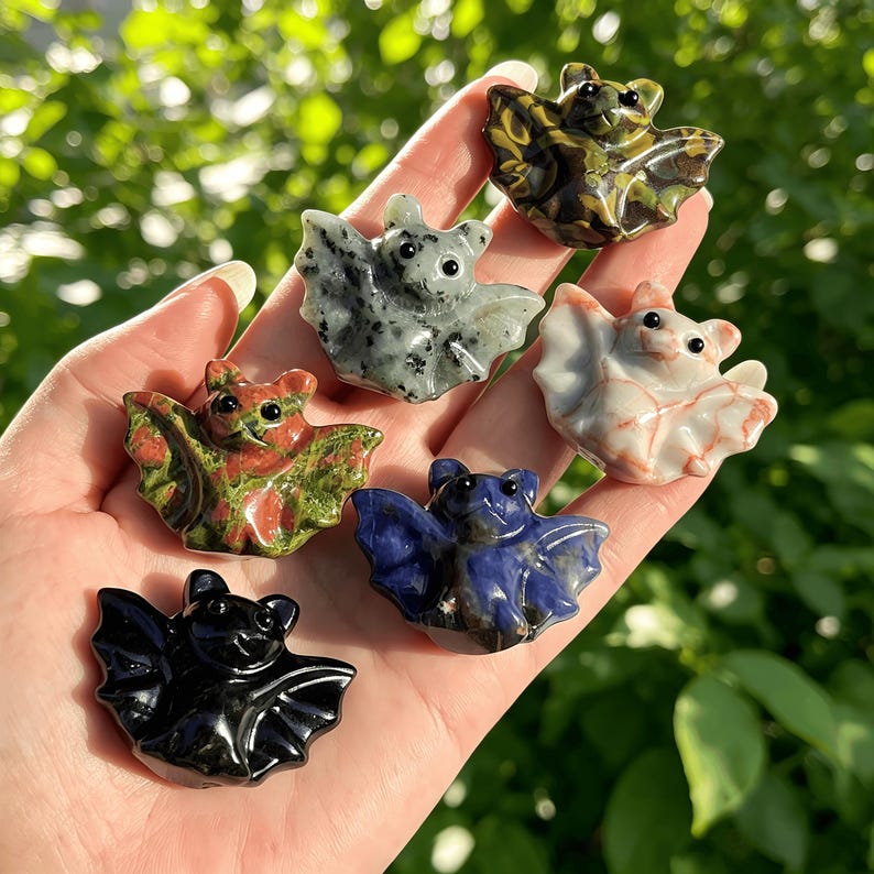 Puede incluir: Una colecci&oacute;n de peque&ntilde;as figuras de murci&eacute;lagos talladas en varios colores y patrones. Los murci&eacute;lagos est&aacute;n hechos de diferentes tipos de piedra, incluyendo negro, verde, azul y blanco. Cada murci&eacute;lago tiene alas detalladas y ojos peque&ntilde;os y redondos.
