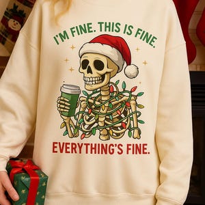 May include: Cream-colored sweatshirt with a humorous Christmas design. It features a skeleton wearing a Santa hat, holding a coffee cup, and wrapped in Christmas lights. The text reads "I'M FINE. THIS IS FINE. EVERYTHING'S FINE."