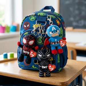May include: A blue backpack featuring superhero designs, with attached plush keychains of Spider-Man, Captain America, and Black Panther. The keychains are labelled "Terry", "Kieran", and "Carl". The backpack is on a wooden desk.