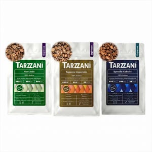Könnte beinhalten: Drei weiße Kaffeeverpackungen der Marke Tarzzani, jeweils mit einem kreisförmigen Haufen gerösteter Kaffeebohnen oben. Die Beutel sind grün, braun und blau, beschriftet mit New Jade, Topazio Imperiale und Spinello Cobalto, alle 100% Arabica.