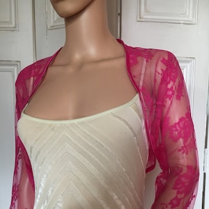 May include: A hot pink lace shrug with a satin trim. The shrug has a scoop neckline and three-quarter sleeves.