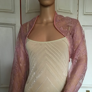 May include: A pink lace shrug with satin trim. The shrug has a scoop neckline and three-quarter sleeves.