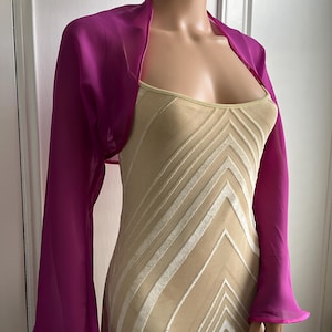 Könnte beinhalten: Eine fuchsia-rosa Chiffon-Schal mit langen Ärmeln und einem glockenförmigen Saum.