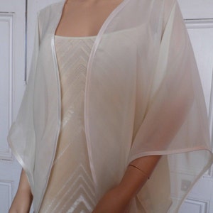 Puede incluir: Un chal de gasa de seda blanca con ribete de satén. El chal está drapeado sobre un maniquí y tiene un aspecto fluido y elegante.