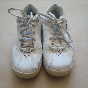 Puede incluir: Par de zapatillas deportivas Fila blancas con cordones. Las zapatillas tienen el logotipo de Fila en la leng&uuml;eta y el lateral. Las zapatillas son de cuero y tienen suela de goma.