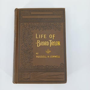 May include: A vintage hardcover book titled "Life of Bayard Taylor" by Russell H. Conwell. The book has a brown cover with gold lettering and decorative floral and geometric designs. The book's spine is also brown.