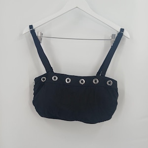 May include: A black cropped top featuring a straight neckline with a row of silver-toned metal grommets across the upper chest. The garment includes two adjustable black shoulder straps and a gathered, slightly puffed bodice design.