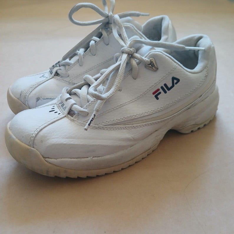 Puede incluir: Par de zapatillas deportivas Fila blancas con cordones blancos. Las zapatillas tienen una suela gruesa y el logotipo de Fila en azul marino y rojo. Las zapatillas est&aacute;n hechas de un material similar al cuero y muestran signos de desgaste.