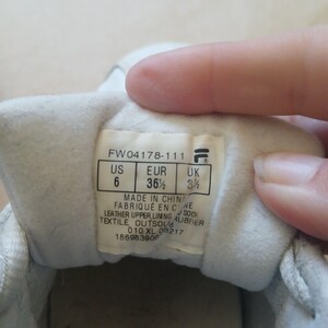 Puede incluir: Primer plano del interior de una zapatilla blanca, que muestra una etiqueta con informaci&oacute;n de tallas. La etiqueta indica la talla EUR 36 1/2, US 6 y UK 3 1/2. La etiqueta tambi&eacute;n incluye el logotipo de la marca y detalles de fabricaci&oacute;n.