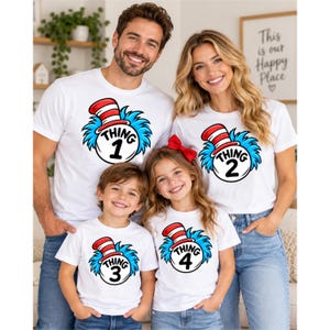 May include: Four white t-shirts featuring a graphic of a red and white striped hat atop a blue fuzzy creature with a circular emblem containing the text Thing 1, Thing 2, Thing 3, or Thing 4. The shirts are worn by a family of four.