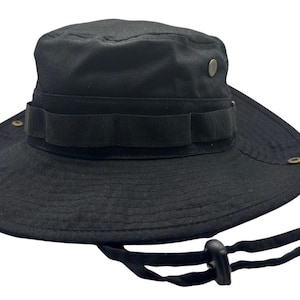 Op de afbeelding: Een effen zwarte bucket hat met een brede rand, een stoffen band met lussen rondom en metalen ventilatiegaatjes aan de zijkanten. De hoed is voorzien van een verstelbare zwarte kinband met een kunststof koordstopper voor een goede pasvorm.