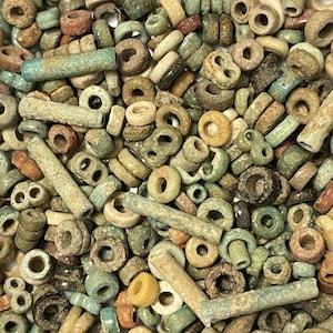 May include: A collection of small, antique beads in various shapes and sizes. The beads are primarily in shades of green, brown, and beige, with some showing signs of wear. The assortment includes round, tube, and other unique shapes, suggesting a vintage or handcrafted origin.