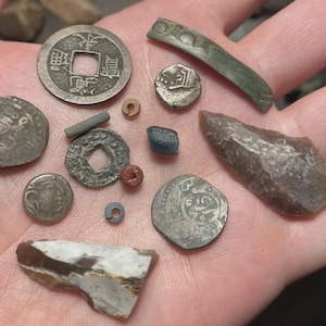 May include: A collection of antique coins and artifacts, including a Chinese coin with square hole, various round coins, a small blue stone, and a piece of flint. The items are in various shapes and sizes, with visible wear and tear.
