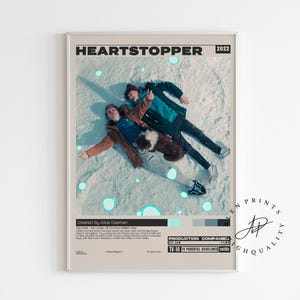 May include: A framed poster featuring the title "HEARTSTOPPER" and the year "2022". The image shows two people lying in the snow. The poster has a light beige border and includes text at the bottom.