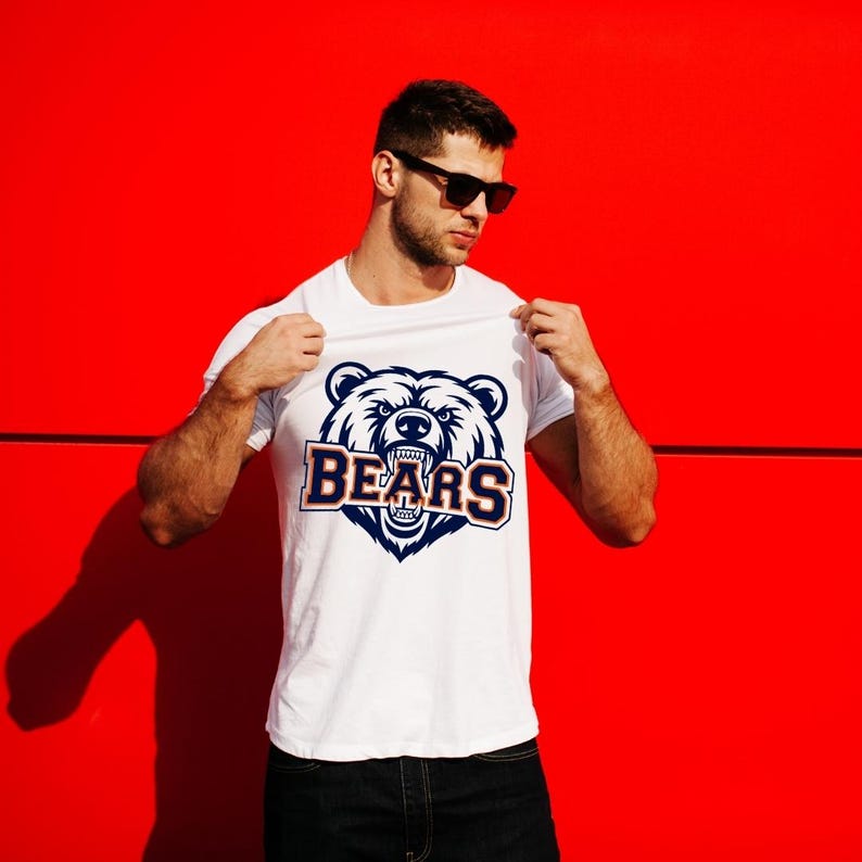 May include: White t-shirt with a navy and orange bear graphic and the word "BEARS". The design is set against a bright red background. The bear graphic has detailed fur and teeth. The t-shirt is being held up.