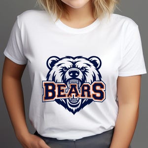 May include: White t-shirt with a navy blue and orange bear head graphic and the word "BEARS". The bear graphic has a fierce expression. The shirt is a classic crew neck style, suitable for casual wear.