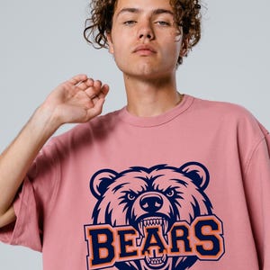 May include: A dusky pink t-shirt with a navy and orange bear head graphic and the word "BEARS". The design is centered on the front of the shirt.