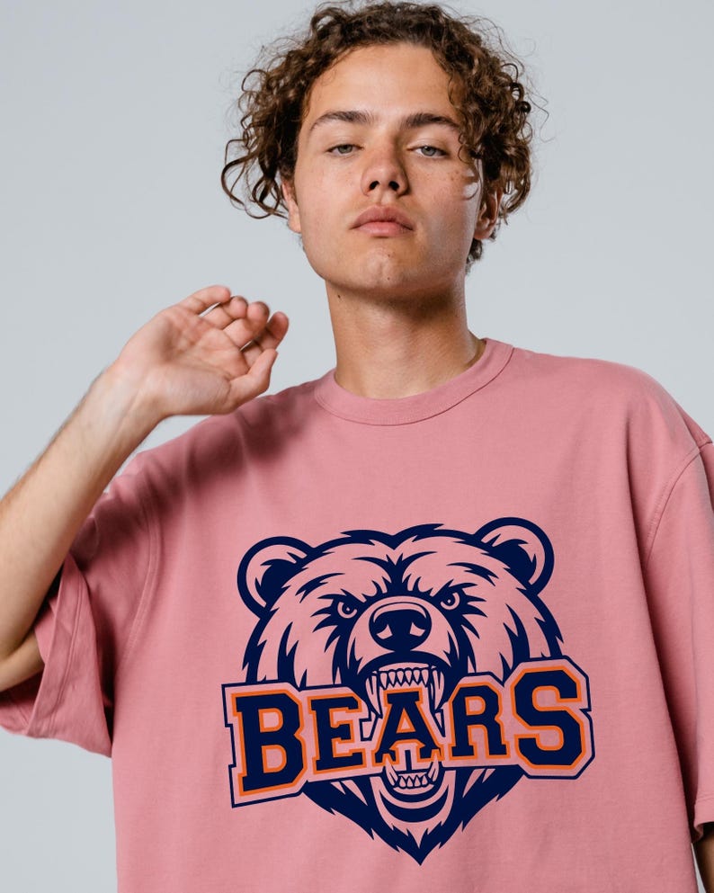 May include: A dusky pink t-shirt with a navy and orange bear head graphic and the word "BEARS". The design is centered on the front of the shirt.