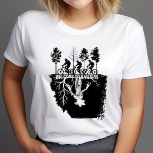 Op de afbeelding: Wit T-shirt met een zwart grafisch ontwerp uit de tv-serie Stranger Things. Het ontwerp bevat silhouetten van mensen op fietsen, bomen en de tekst "WELCOME TO HAWKINS". Hieronder een afbeelding van een monster.
