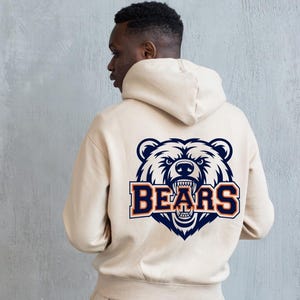 May include: A beige hooded sweatshirt featuring a navy blue, white, and orange bear graphic on the back, with the word "BEARS" beneath. The hoodie has a drawstring and a kangaroo pocket.