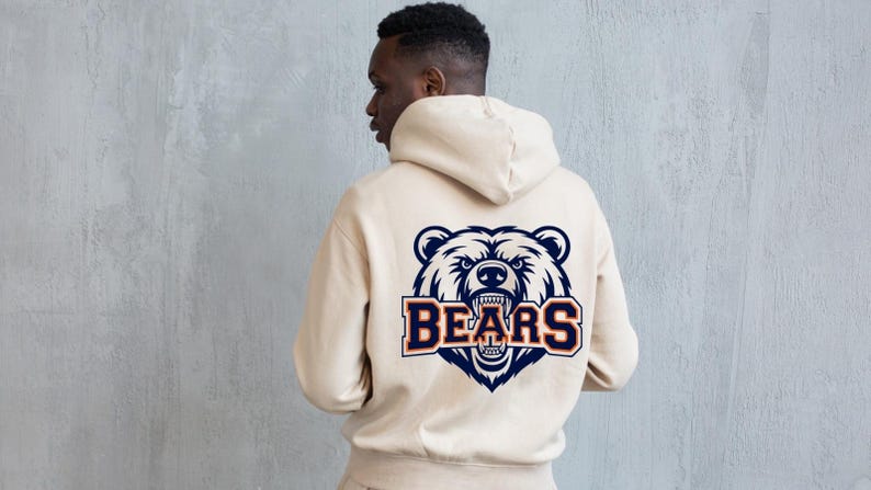 May include: A beige hooded sweatshirt featuring a navy blue, white, and orange bear graphic on the back, with the word "BEARS" beneath. The hoodie has a drawstring and a kangaroo pocket.