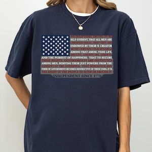 May include: Navy blue t-shirt featuring an American flag design with the text of the Declaration of Independence. The shirt includes the phrase "Independent Since 1776". A patriotic apparel item.