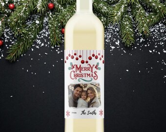 May include: A clear wine bottle with a custom label featuring a family photo and the words "Merry Christmas." The label is decorated with red berries and snowflakes. The background includes evergreen branches and red ornaments.