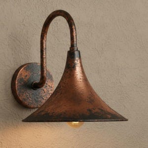 Puede incluir: Una lámpara de pared de color cobre. La lámpara tiene un brazo curvo y una pantalla en forma de campana, con un acabado texturizado. La luz está montada sobre una base circular y el diseño evoca una estética vintage.
