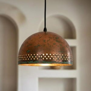May include: A copper pendant light with a dome-shaped shade. The shade has a diamond-shaped pattern around the bottom edge and a warm, golden interior. The light hangs from a black cord.