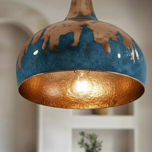 May include: A pendant light fixture with a copper-colored interior and a blue and copper exterior. The light bulb is visible inside the fixture. The fixture is hanging from the ceiling.