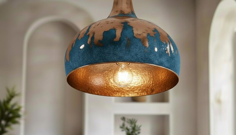 May include: A pendant light fixture with a copper-colored interior and a blue and copper exterior. The light bulb is visible inside the fixture. The fixture is hanging from the ceiling.