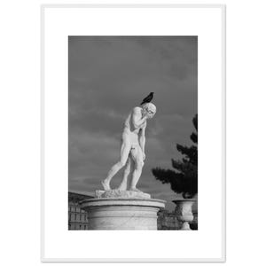 Könnte beinhalten: Schwarz-Weiß-Fotografie einer klassischen Statue eines Mannes, mit einem Vogel auf seinem Kopf. Die Statue steht auf einem runden Sockel, mit einem bewölkten Himmel im Hintergrund. Ein Baum und ein Gebäude sind ebenfalls zu sehen.