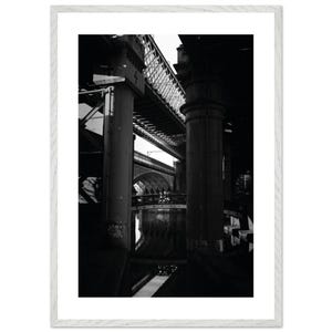 May include: Black and white photograph of a complex network of bridges and support structures. The image is framed in a white wooden frame. The composition emphasizes the interplay of light and shadow, creating a dramatic effect.
