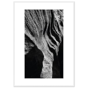 May include: Black and white photograph of a rock formation with textured, layered patterns. The image captures the natural curves and shadows of the stone, creating a dramatic contrast. The artwork is framed in a white border.