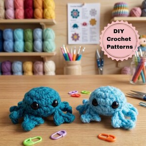 May include: Two small crocheted octopus figures, one in dark teal and one in light blue, each featuring large black safety eyes. Scattered around the figures on the wooden surface are several colorful plastic stitch markers in various shapes.