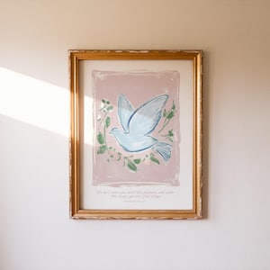 Pode incluir: Uma impressão de arte emoldurada com uma pomba azul clara com asas abertas, cercada por folhagens verdes, em um fundo rosa. A impressão está em uma moldura dourada, com texto na parte inferior.