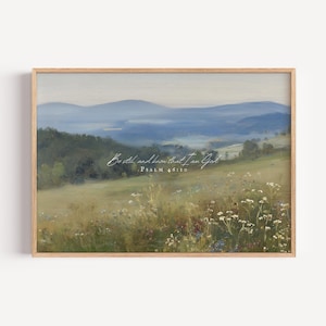 Könnte beinhalten: Ein gerahmter Landschaftsdruck mit einer ruhigen Berglandschaft in Blau- und Grüntönen. Der Vordergrund zeigt ein Feld mit Wildblumen. Der Text "Be still and know that I am God" und "Psalm 46:10" ist auf dem Druck geschrieben.