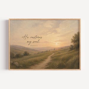 May include: Framed landscape art print featuring a path winding through a grassy field towards a sunset. The artwork includes the text "He restores my soul" and "Psalm 23:3" in a handwritten style. The frame is a light wood color.