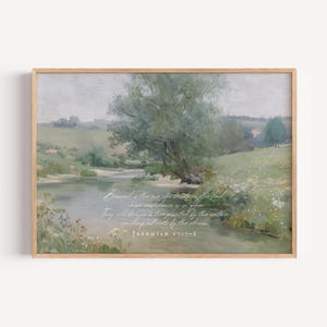 May include: A framed print of a tranquil landscape painting. The artwork shows a river scene with a large tree, grassy banks, and rolling hills. The text "Blessed is the one who trusts in the Lord..." is written in script. The frame is a light wood colour.