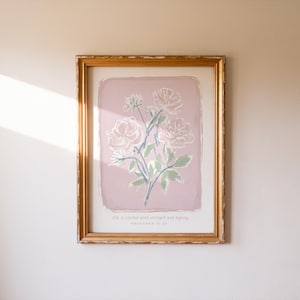 Peut inclure: Une impression florale encadrée avec un bouquet de roses rose clair et des feuilles vertes sur fond rose. L'œuvre est dans un cadre doré et comprend le texte "She is clothed with strength and dignity PROVERBS 31:25."