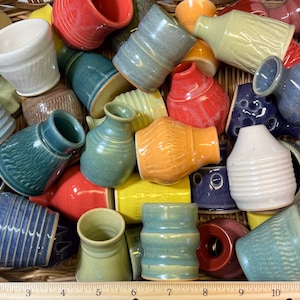 May include: A collection of small, handmade ceramic vases in various colors and patterns. The vases are arranged in a wicker basket.